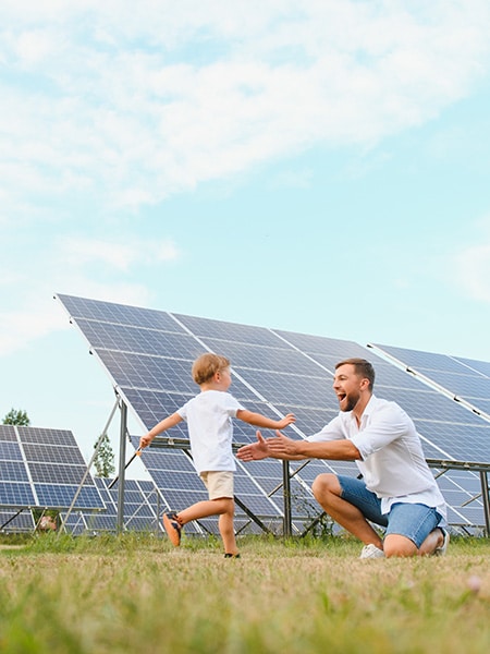 Bambino corre nelle braccia del padre, felice perchè circondato da pannelli solari